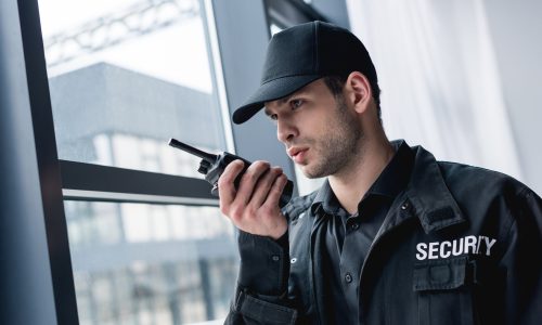 cropped view of guard in uniform talking on walkie-talkie and looking away